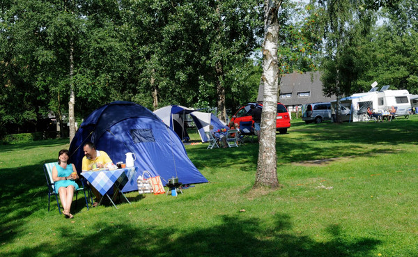 Ein Zelt steht auf der Wiese, zwei Camper sitzten davor